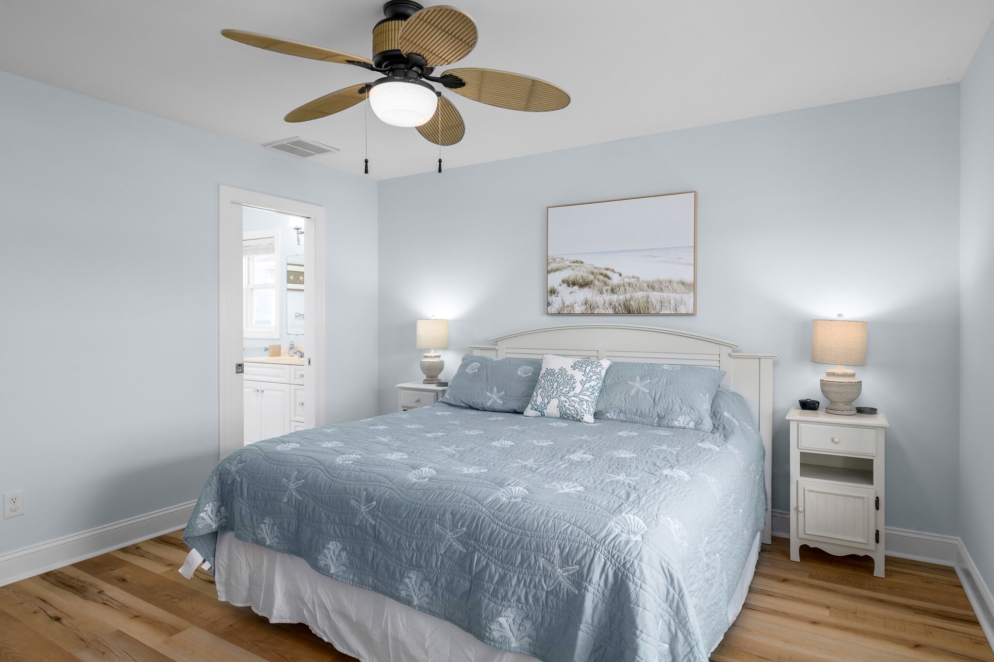 A bedroom with a bed, two bedside tables, a ceiling fan, and a wall-mounted lamp.