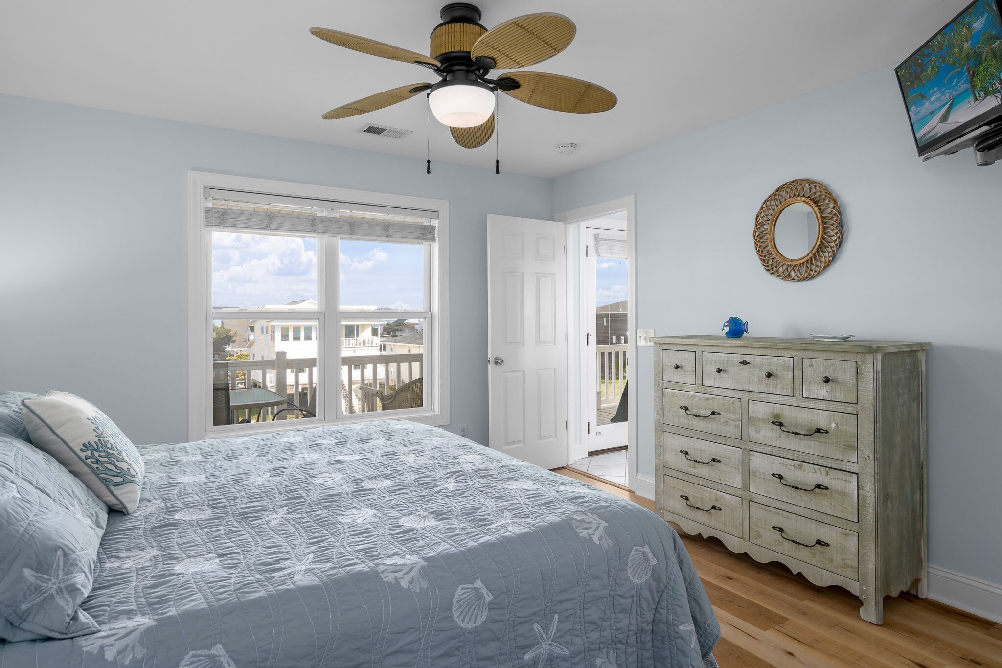 A bedroom with a bed, a dresser, a ceiling fan, a TV, and a balcony door.