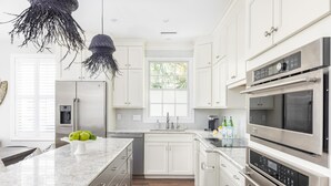 A modern kitchen with white cabinetry, stainless steel appliances, and a marble countertop. - Designer's Dream in Historic Charleston +Walk to King St and Dining (Charleston)