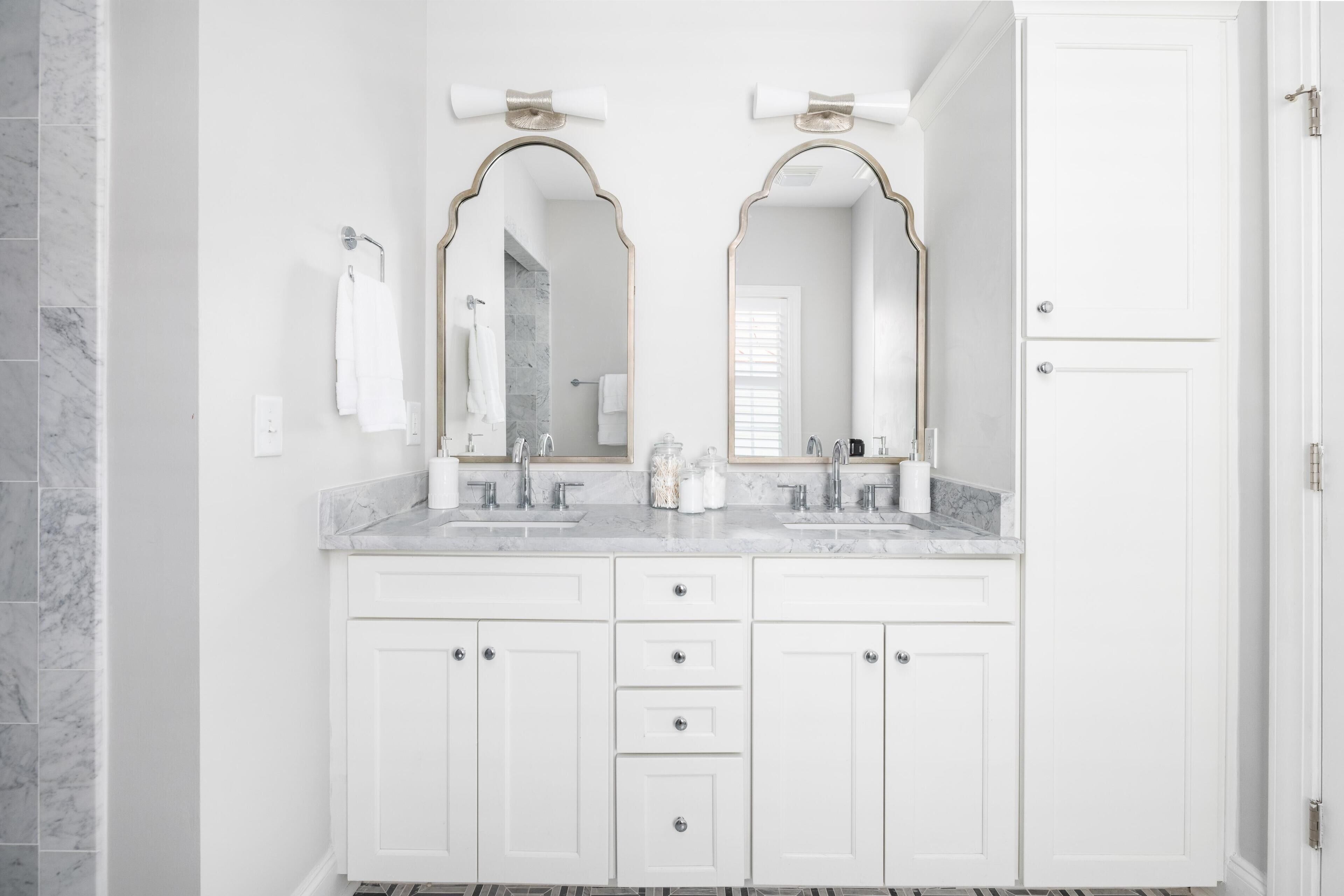 A bathroom with white cabinetry, two sinks, and a large mirror.
