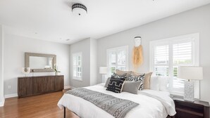 A bedroom with a large bed, a dresser, a mirror, and two windows with blinds. - Designer's Dream in Historic Charleston +Walk to King St and Dining (Charleston)