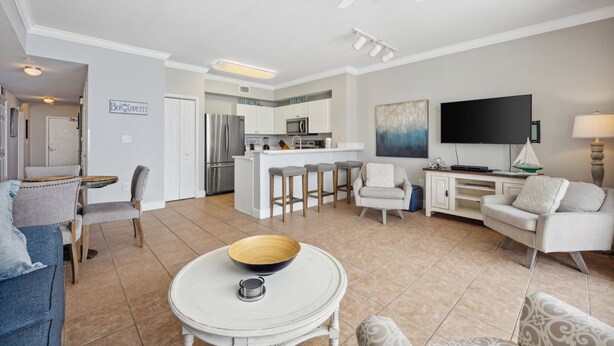 A modern living room with a central island, a dining area with a round table, and a kitchen with a bar area. - Tidewater 1413 - 2198668 (Panama City Beach)