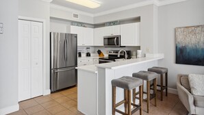 A modern kitchen with white cabinetry, stainless steel appliances, and a central island with stools. - Tidewater 1413 - 2198668 (Panama City Beach)