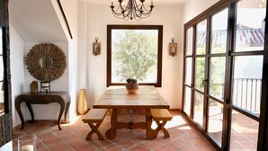 Un coin repas comprenant une table en bois, des bancs, un lustre, une grande fenêtre et un miroir décoratif.