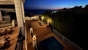 Une terrasse sur le toit avec une piscine, des sièges extérieurs et une vue sur la mer au crépuscule.