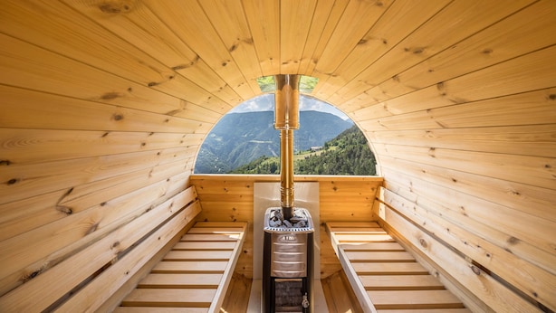 A wooden cabin with a wood-burning stove, wooden benches, and a view of mountains. - Apartment "Thalerhof Sancta Sebastianus" with Mountain View, Garden & Wi-Fi (Unterinn Ritten)