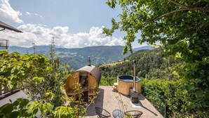 A wooden cabin with a hot tub and outdoor seating, surrounded by trees and a mountainous landscape. - Apartment "Thalerhof Sancta Sebastianus" with Mountain View, Garden & Wi-Fi (Unterinn Ritten)