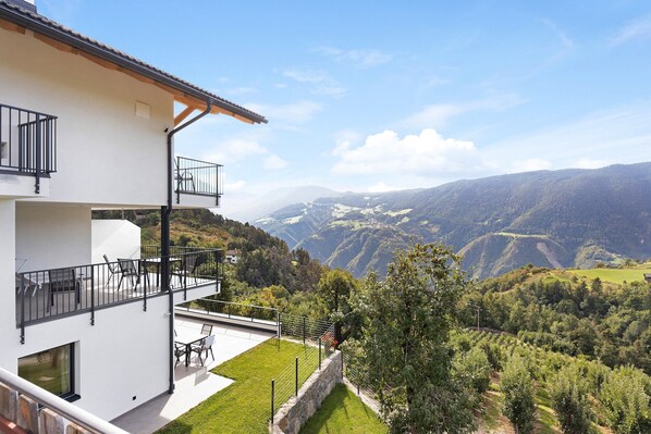 Un bâtiment moderne à deux étages, doté d’un balcon, d’un espace extérieur aménagé pour s’asseoir et offrant une vue sur un paysage montagneux.