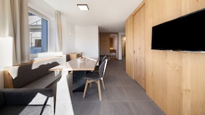 Habitació moderna amb paret de fusta, televisió de pantalla plana, taula de dinar amb cadires i un sofà.