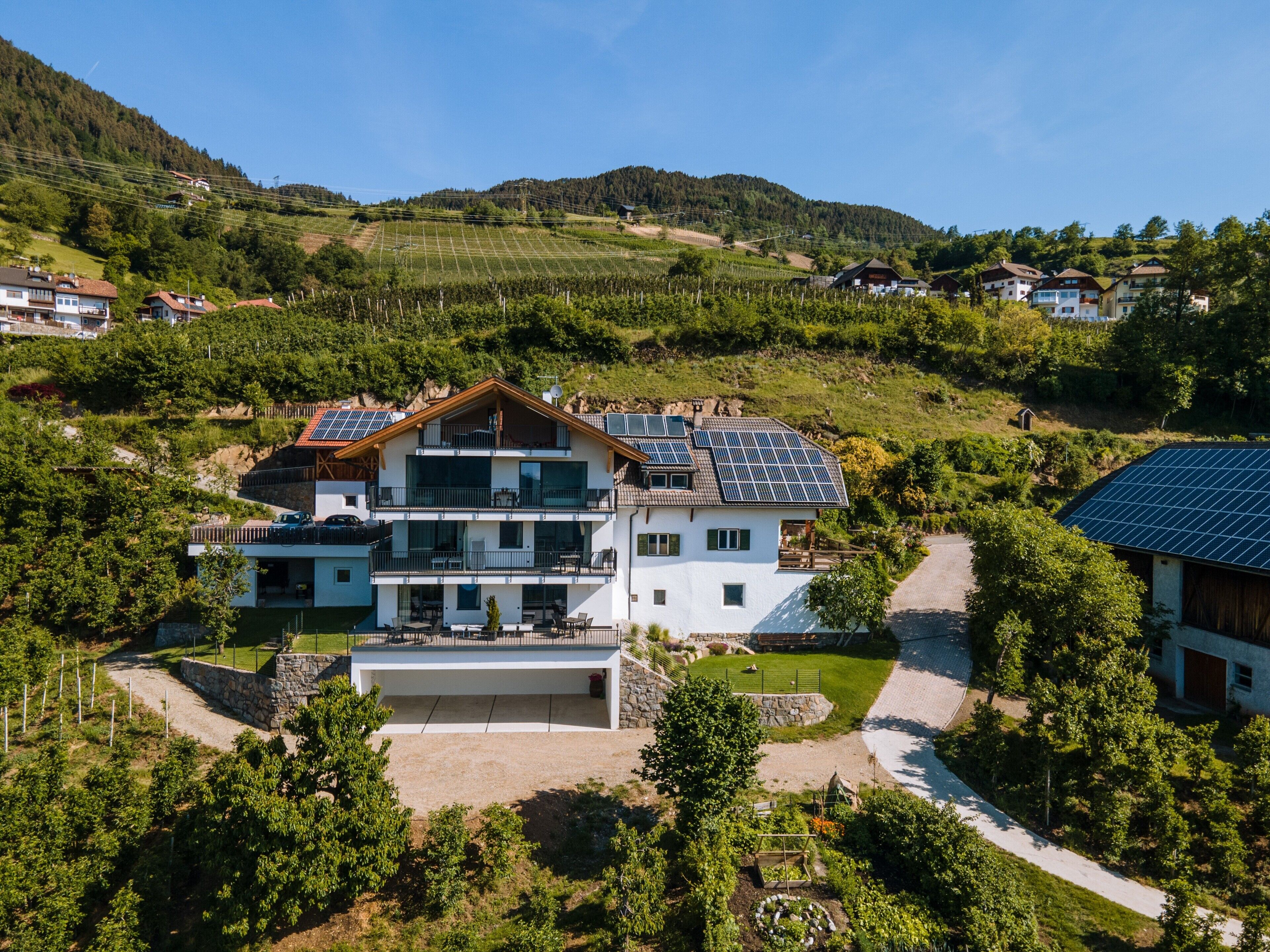 Ein großes, zweistöckiges Haus mit Garage, umgeben von üppiger Vegetation und Hügeln.