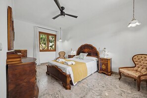 Une chambre à coucher avec un lit, des meubles en bois, un ventilateur de plafond et une fenêtre donnant sur un paysage verdoyant.