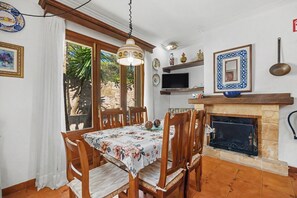 A dining area with a table set for four, wooden chairs, a hanging light fixture, a television, and a fireplace. - Villa Damar with Pool, Garden, Terrace, Balcony, A/C & Wi-Fi (Can Picafort)