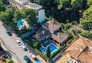 Eine Vogelperspektive zeigt ein Wohnhaus mit Pool, mehrere Autos, die am Straßenrand geparkt sind, und eine Straße, die parallel zum Grundstück verläuft.