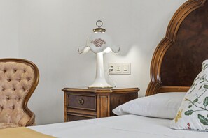 A bedroom with a tufted armchair, a bedside table with a lamp, and a bed with a floral pillow. - Villa Damar with Pool, Garden, Terrace, Balcony, A/C & Wi-Fi (Can Picafort)