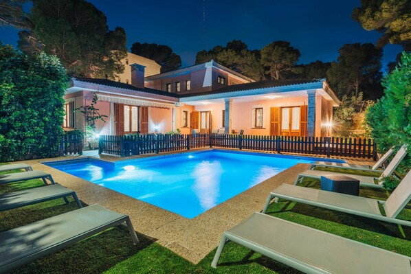 A swimming pool with lounge chairs, a wooden fence, and a house with multiple windows.
