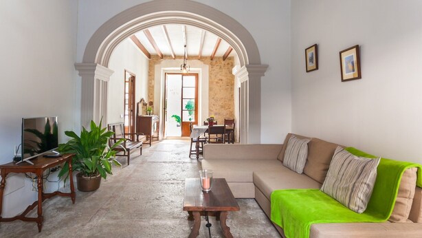 A living room with a sofa, a TV, a table, and a dining area in the background. - Holiday Home Sa Lluna Blava with Pool & Wi-Fi (Santa Margalida)