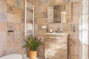 Une salle de bain avec des carreaux décorés, un porte-serviettes blanc, un lavabo avec un miroir et une plante en pot.