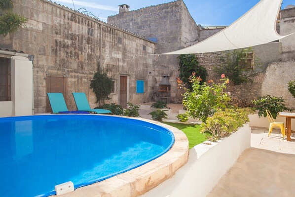 Une piscine avec des chaises longues, un bâtiment en pierre et une pergola offrant de l’ombre.
