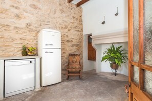 A compact kitchen with a white refrigerator, a wooden chair, a potted plant, and a stone wall.