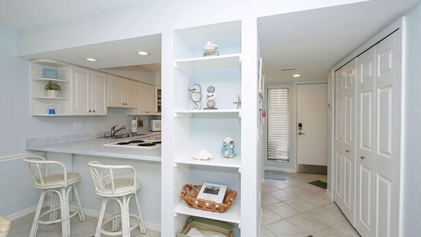 A kitchen with white cabinets, a white countertop, and two wicker chairs. - Runaway Bay Resort by BBG (Bradenton Beach)