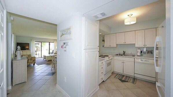 A kitchen with white cabinets, a stove, and a refrigerator. There is a dining area with a table and chairs visible through an open door.