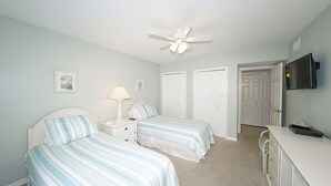 A bedroom with two beds, a ceiling fan, a desk, and a TV. - Runaway Bay Resort by BBG (Bradenton Beach)