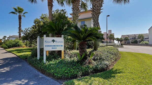 A sign for Sago Sands Condominium 3668, surrounded by lush greenery and palm trees.