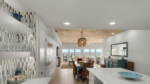 A modern kitchen with white countertops, a dining area with blue chairs, and a view of the ocean through large windows. - Sago Sands 302 - 2340381 (Santa Rosa Beach)
