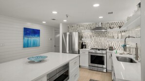 A modern kitchen with white cabinetry, stainless steel appliances, a coffee maker, and a decorative blue painting. - Sago Sands 302 - 2340381 (Santa Rosa Beach)