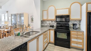 Una cocina moderna con encimeras de granito, armarios de madera, estufa negra y microondas.