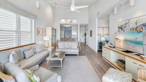 Amplia sala de estar con sofá, mesa de centro y reposapiés, una cocina con una isla grande y un comedor con sillas y mesa.