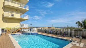 A swimming pool with a clear blue water, surrounded by a brick deck and a white fence. - Sea Dunes 501 (Fort Walton Beach)