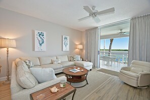 A spacious living room with a sofa, armchairs, a coffee table, and a view of the ocean through large windows. - Harbor Villa Club 206 (Longboat Key)
