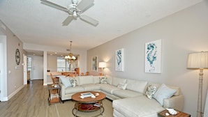 A spacious living room with a large L-shaped sectional sofa, a round coffee table, and a dining area in the background. - Harbor Villa Club 206 - 2129044 (Longboat Key)