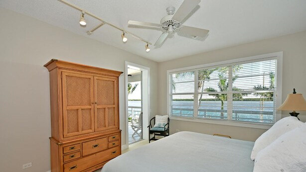 A bedroom with a bed, a wooden wardrobe, a ceiling fan, a window with blinds, and a view of the outdoors. - Harbor Villa Club 206 - 2129044 (Longboat Key)