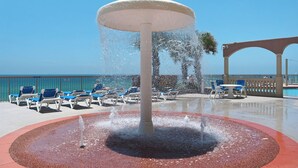 A water fountain surrounded by lounge chairs and a poolside area with a clear view of the ocean. - Sunrise Resort by BBG (Panama City Beach)