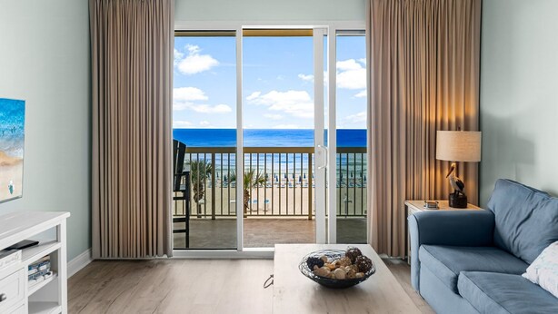 Ein Zimmer mit Balkon, einer Couch, einem Tisch mit Lampe und einem Fernseher.