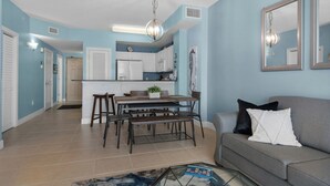 A modern living room with a gray sofa, a coffee table, and a dining area with a wooden table and chairs. - Sunrise Resort by BBG (Panama City Beach)