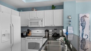 A modern kitchen with white cabinets, a stainless steel sink, a microwave, a stove, and a coffee maker. - Sunrise Resort by BBG (Panama City Beach)