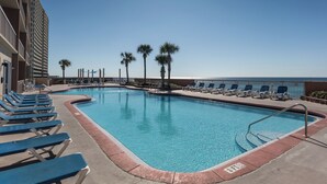 A pool area with lounge chairs, palm trees, and a view of the ocean. - Sunrise Resort by BBG (Panama City Beach)