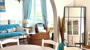 A living room with a blue sofa, white armchairs, a round table, and a cabinet with glass doors. - CANNES VILLA SWIMMING POOL, SEA VIEW,15 MN PALAIS DU FESTIVAL,1 MN BEACH ON FOOT (Cannes)