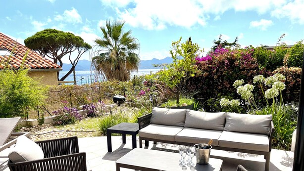 An outdoor seating area with a sofa, chairs, and a table, surrounded by lush greenery and a view of the sea. - CANNES VILLA SWIMMING POOL, SEA VIEW,15 MN PALAIS DU FESTIVAL,1 MN BEACH ON FOOT (Cannes)