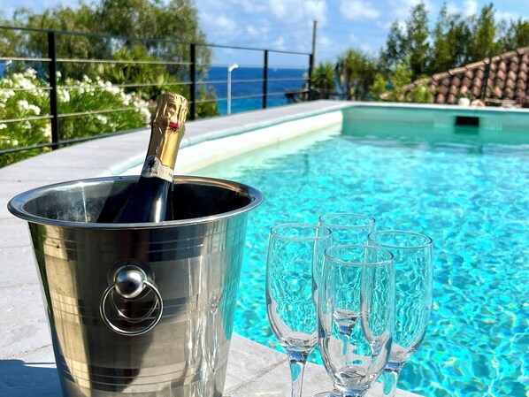 Une scène au bord de la piscine, avec une bouteille de champagne dans un seau en métal et plusieurs verres vides.