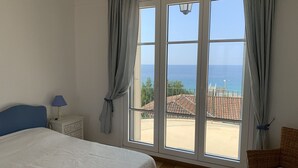 A bedroom with a bed, a nightstand, a lamp, and a view of the sea through large windows. - CANNES VILLA SWIMMING POOL, SEA VIEW,15 MN PALAIS DU FESTIVAL,1 MN BEACH ON FOOT (Cannes)