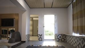 A living room with a TV, seating, a door leading outside, and patterned walls. - Egypt 5 - STAR Cozy 3 BR Villa with Garden (First 6th of October)