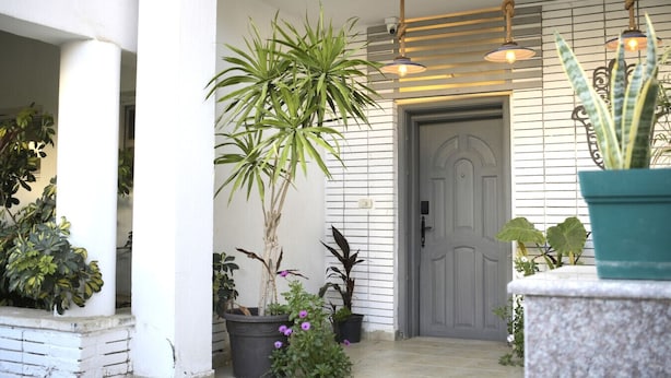 A front porch with a white door, potted plants, and hanging lights. - Egypt 5 - STAR Cozy 3 BR Villa with Garden (First 6th of October)