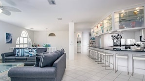 A modern kitchen with a bar area, a grey sofa, and a dining table. - Vaca Cut Sunsets 5 bed 4 bath home with pool Gulf Views on Vaca Cut (Marathon)