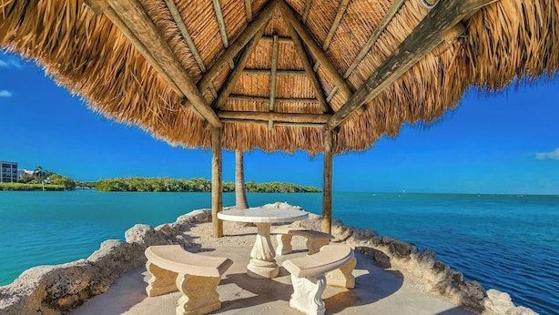 A thatched-roof structure with a table and benches, overlooking a clear blue sea. - Vaca Cut Sunsets 5 bed 4 bath home with pool Gulf Views on Vaca Cut (Marathon)