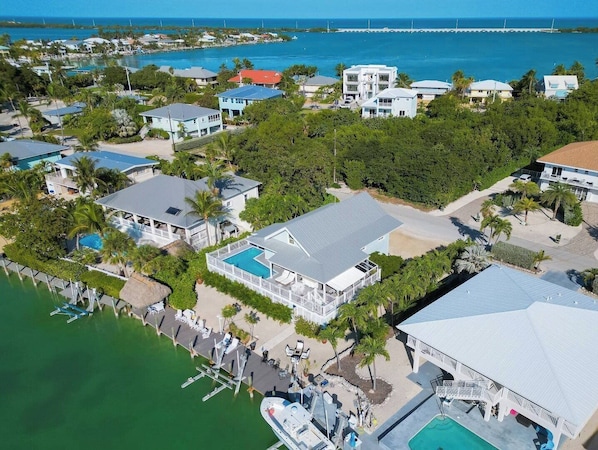 An aerial view of a coastal resort with multiple buildings, a marina, and a large swimming pool.