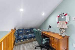 A room with a blue sofa, a green office chair, a wooden desk, and a wall-mounted lamp.